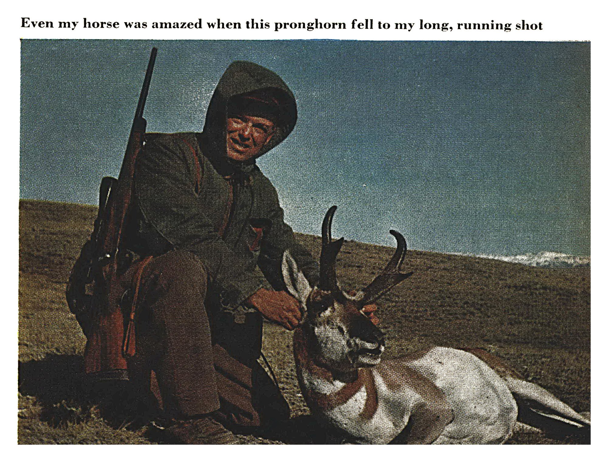 A smiling hunter in a hooded parka kneels on a grassy slope with his rifle slung over his shoulder, holding the head of a pronghorn buck.