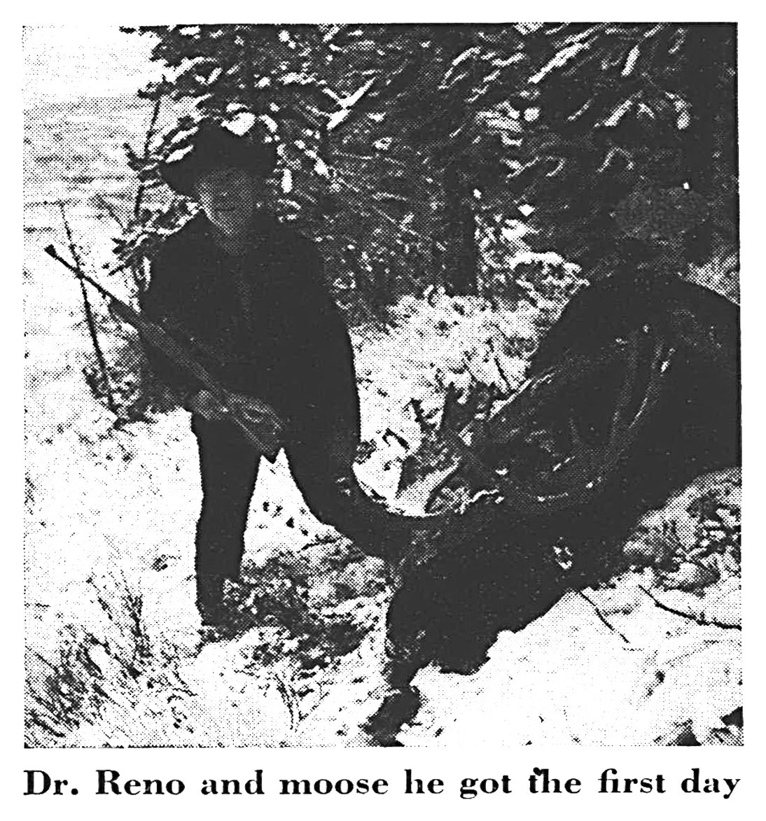 Black-and-white photo of a hunter holding a rifle beside a downed bull moose in snowy timber.