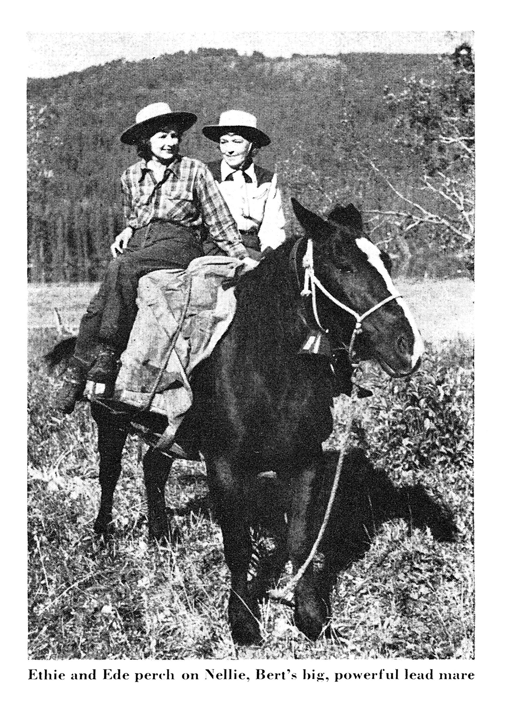 Black-and-white photo of two women in wide-brimmed hats riding double on a large dark horse in a mountain meadow.